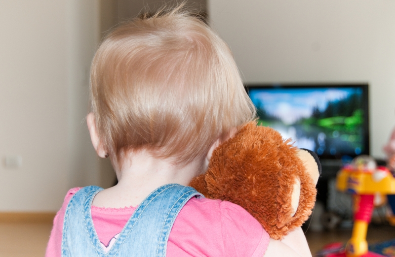 Ребенок смотрит телевизор с игрушкой в обнимку