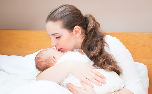 Молодая мама целует младенца